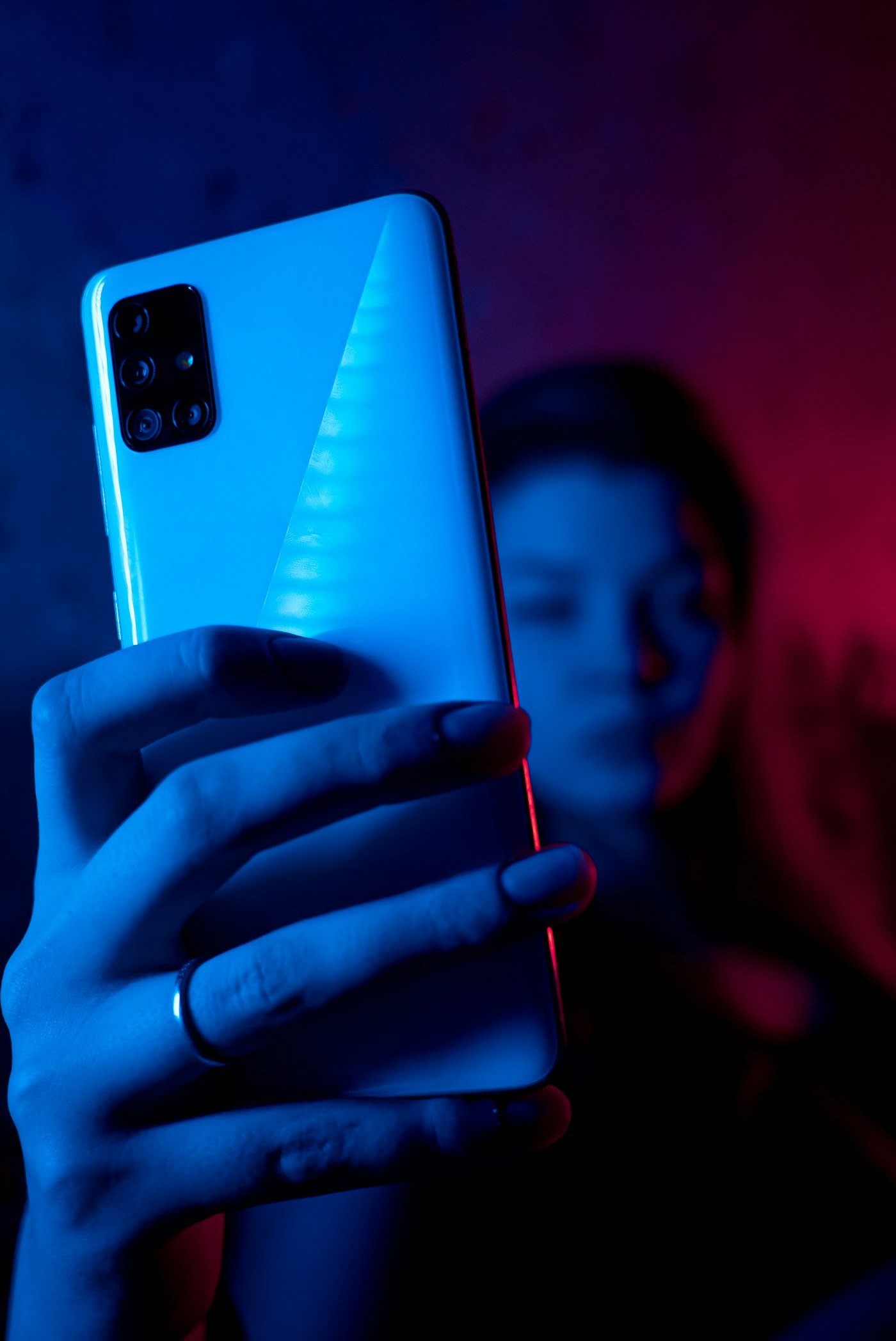 Main tenant un smartphone sous une lumière néon bleue et rouge